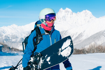 Snowboarder woman standing with snowboard in beautiful mountain peaks covered with snow on...