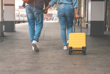 Happy loving couple with luggage and backpack walking along railway platform as they are ready to...