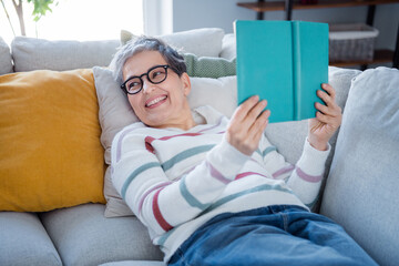 Photo of positive lovely person laying couch hold opened book look away imagine pastime modern...