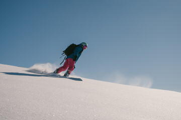 female snowboarder riding on slope of powdery snow in high mountains. Freeride at ski resort