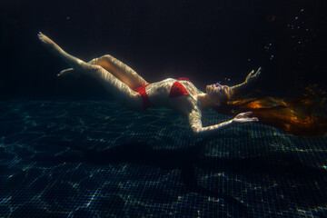 A beautiful sporty girl poses underwater with loose hair against the bright rays of the sun from...
