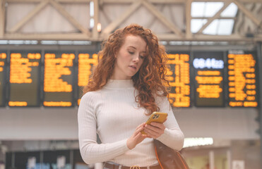 an excited redhead female holding a smartphone while at the train station and the train is...