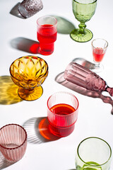 Glasses of different colors with drinks with shadow from sunlight. Summer alcoholic drinks