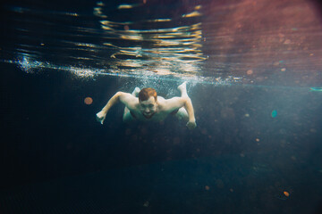 A young man swims in a pool, underwater. Concept of vacation and carefree life.