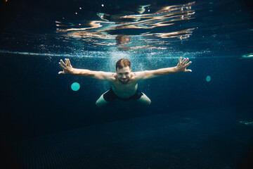 A young man swims underwater in a pool. Summer vacation concept.