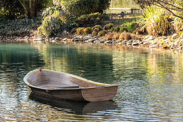 A small wooden rowing boat floats on calm waters with reeds in the water. Reflections of the boat...