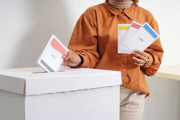 Close up of Asian hijab woman inserting and putting the voting paper into the ballot box. General elections or Pemilu for the president and government of Indonesia. Isolated image on white background