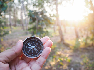 Close up of compass in woman hand with forest in the sunset time as background. The concept of...