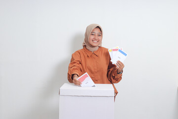 Portrait of Asian hijab woman inserting and putting the voting paper into the ballot box. General...