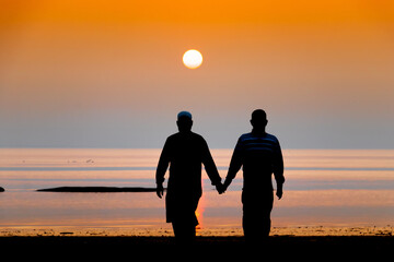 Silhouette view of two Muslim men walking hand in hand on a sea beach during twilight sunset. Friendship is an immortal concept even in old age.
