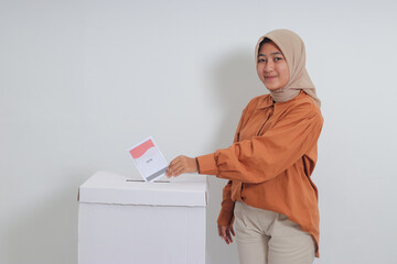Portrait of Asian hijab woman inserting and putting the voting paper into the ballot box. General...