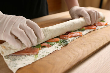 Obraz premium Lavash with filling is wrapped in a roll. Preparation of a roll with cheese, fish and vegetables