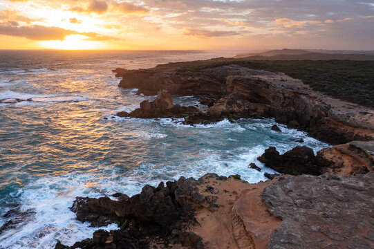 A dramatic sunset over waves crashing on a rugged coastline