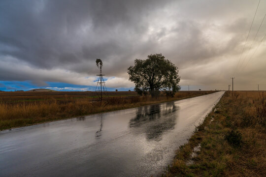 Rain falling from a dramatic stormfront over a long straight country road