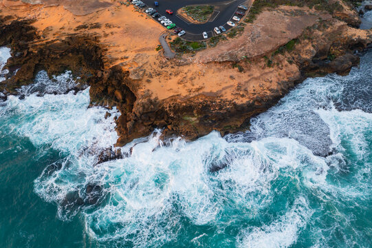Aerial view waves crashing on a rugged coastline with a lookout carpark - Powered by Adobe
