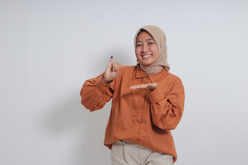 Portrait of Asian hijab woman showing the little finger dipped in purple ink after the voting for general election or Pemilu for the president and government of Indonesia. Isolated on white background