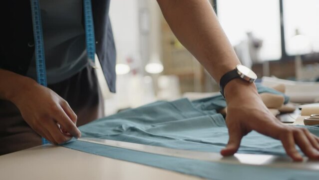 Professional tailor chalking sewing pattern onto fabric before cutting a piece in a dressmaking workshop. Tilt-up shot