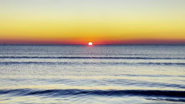 Golden Horizon: A Sea Sunrise | The photo captures a breathtaking view of a sunrise over the sea. The sun is visible as a bright orb near the center of the image. The sky transitions from dark blue at