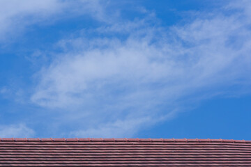 Red tile roof top on blue sky with cloud background.