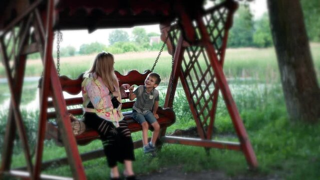 Mom with child boy kid rides on a swing and have fun talking in idyllic family place 