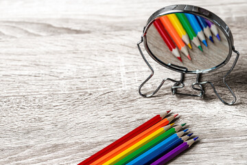 Colored pencils on the table are reflected in the mirror. Rainbow style. Selective focus.