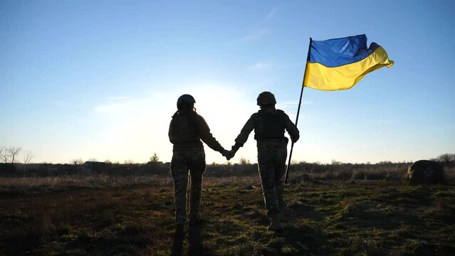 Soldiers of ukrainian army runs with Ukraine flag and holds hands of each other. People in military uniform holding waving flag as symbol of victory against russian aggression. End of war concept
