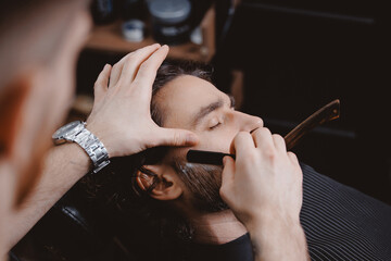 Closeup barber shaving man with sharp steel razor, barbershop warm retro old toning