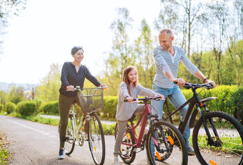 Obraz premium Smiling father and mother with daughter during summer outdoor bicycle riding. They enjoy togetherness in the summer city park. Happy parenthood and childhood or active sport life concept image.