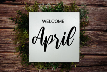 Welcome April text message with green leaf decoration on wooden background - obrazy, fototapety, plakaty