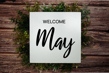 Welcome May text message with green leaf decoration on wooden background