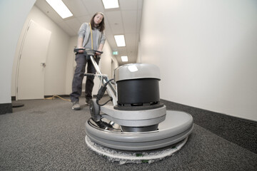 cleaner using a buffer machine to clean a carpet in a hallway