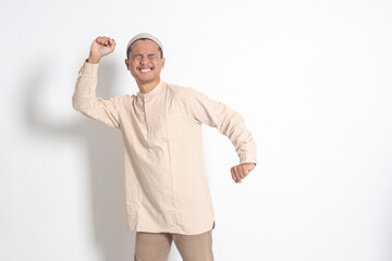 Portrait of overworked Asian muslim man in koko shirt with skullcap stretching his hands and body...