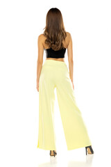 Fashion model posing in black blouse, yellow loose pants and high heel shoes. Rear view on a white background