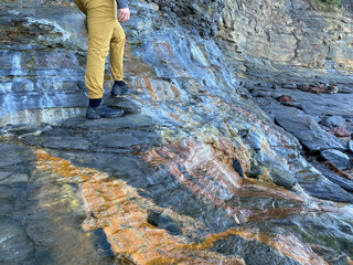 Climber on multicolored rocks. Hiker walking on a colorful rock face. Close-up on the man's legs and the wet stones.