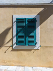 Window with closed green shutters, ochre wall, light and shadow. Bastia, Haute-Corse, France.
