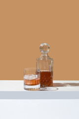 Vaso de whisky con hielo y decantador sobre fondo naranja