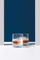 Dos vasos de whisky con hielo sobre un fondo azul