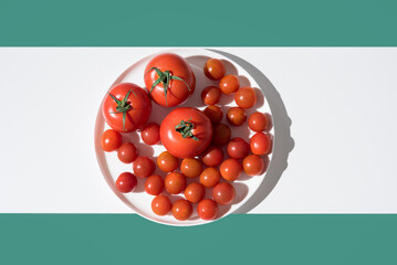 Tomates maduros frescos variados en un plato blanco sobre fondo verde. Vista superior	