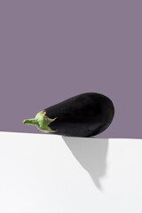 Una berenjena fresca sobre un soporte blanco y fondo morado
