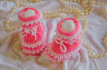 Pink knitted booties on light background with beads
