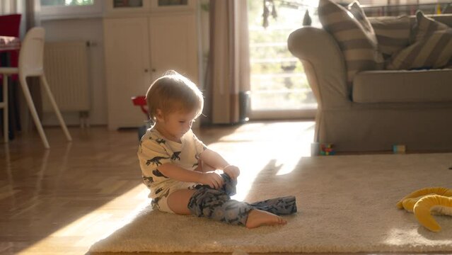 A toddler sits on the floor, engaging with a toy snake by holding, moving, and exploring its features.