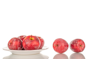 Several red sweet apples on a ceramic white saucer, macro, isolated on white background.