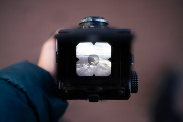 Zdjęcie aparatu analogowego. Fotograf trzyma aparat robiąc zdjęcie plaży o wschodzie słońca - 726633668