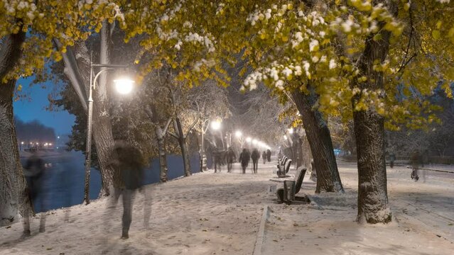 Picturesque timelapse of the illuminated Uzhgorod embankment during heavy snowfall, people walk, play and enjoy the first snow.