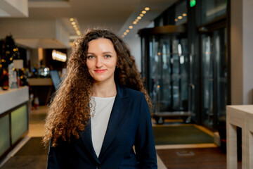 smiling curly female employee stands in the hotel lobby staff manager or receptionist hospitality