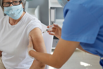 Nurse or doctor holding syringe and giving vaccine shot to old lady in surgical face mask. Retired senior woman getting antiviral injection at vaccination center during infectious disease epidemic