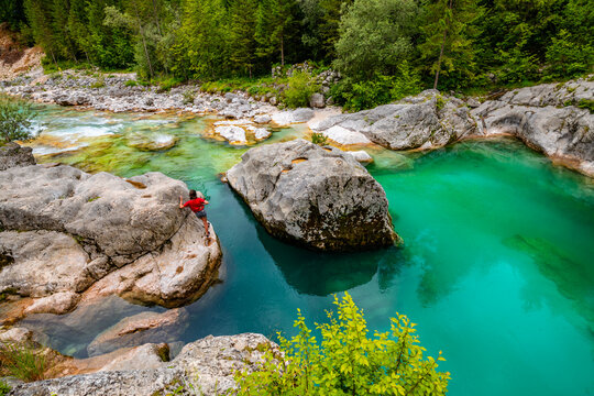 Soča or Isonzo River (Emerald River) in Slovenia, a wild alpine river with crystal clear water and perfect turquoise green color. Rapids, and cascades and deep green pools. Girl with red shirt on rock