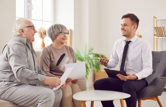 Happy laughing senior couple talking with financial agent about health insurance in retirement sitting on sofa at home. Elderly man and woman meeting with advisor going to sign investment contract.