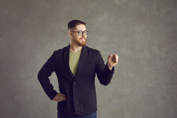 Young person demonstrating stuff. Happy man showing invisible object. Positive hipster guy in suit and glasses holding something like cup or beverage bottle. Concept of people advertising new product - Powered by Adobe