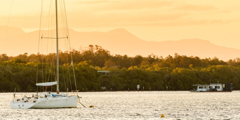 Sailboats anchored on the river close to the shore overlooking the mangrove forest and mountains,...